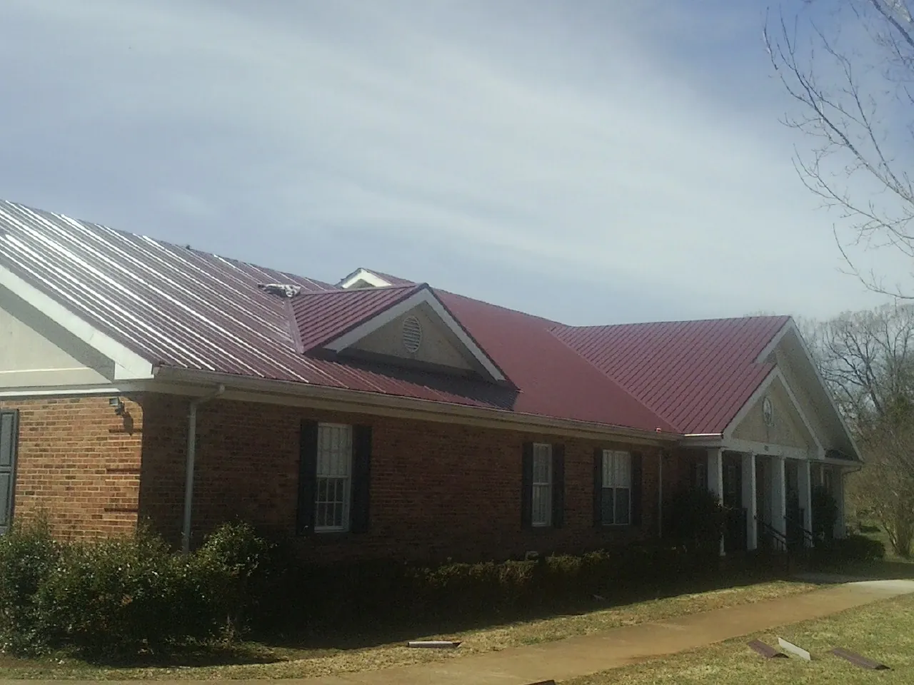 Red metal roof with gabled entries on a long brick building, from a Hail Damage Roof Repair job in Bellmawr