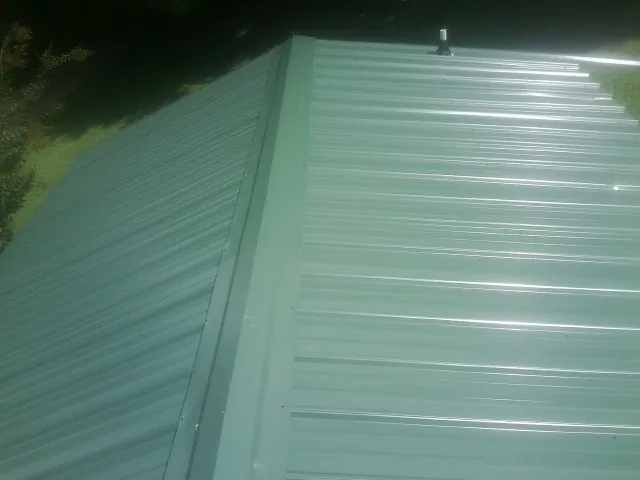 New green metal panels meeting at the ridge of a roof — Flat Roof Repair work by our crew in Bellmawr