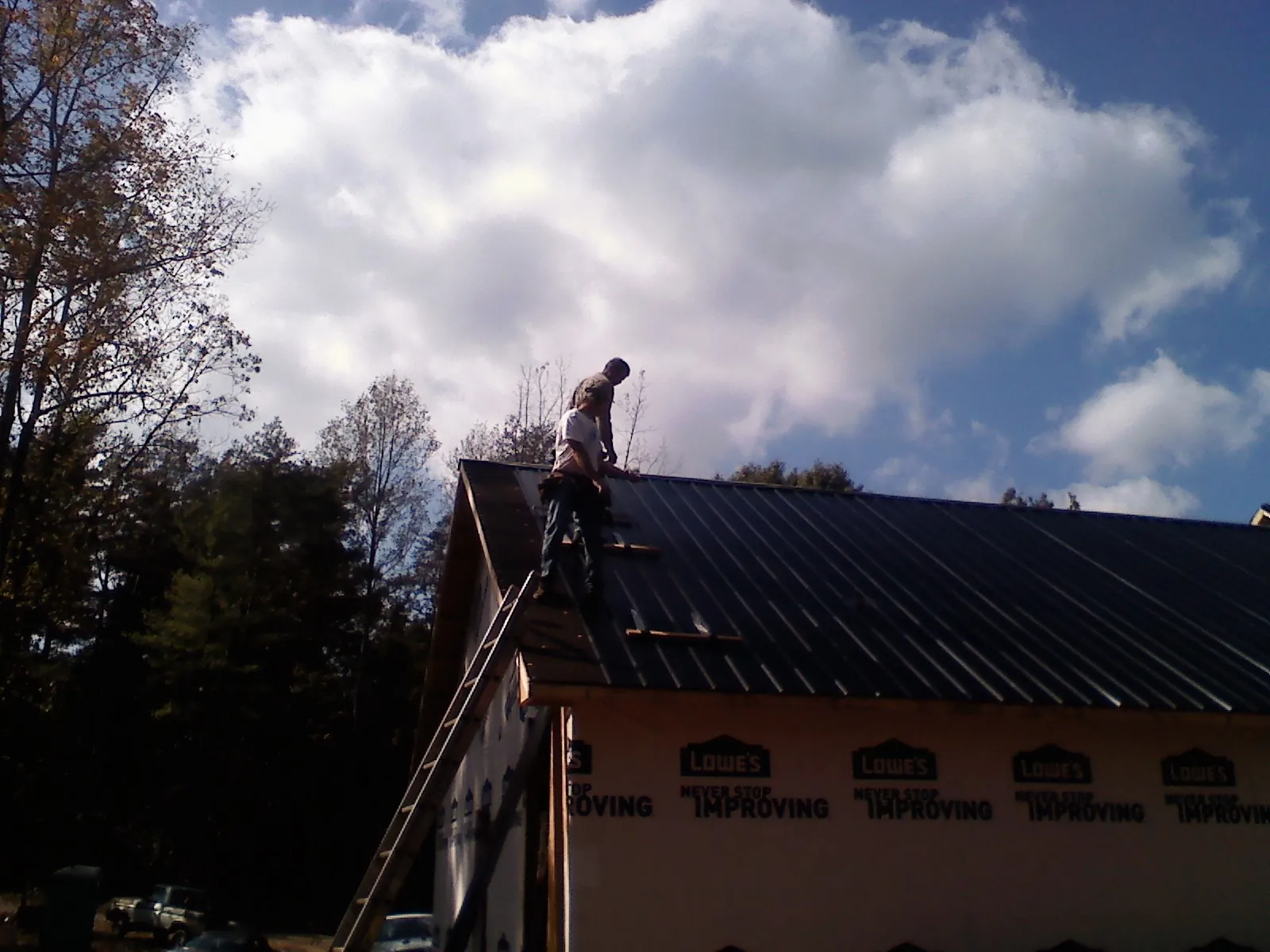 Roofer fastening dark metal panels high against a cloudy sky, from a Roof Inspection job in Bellmawr