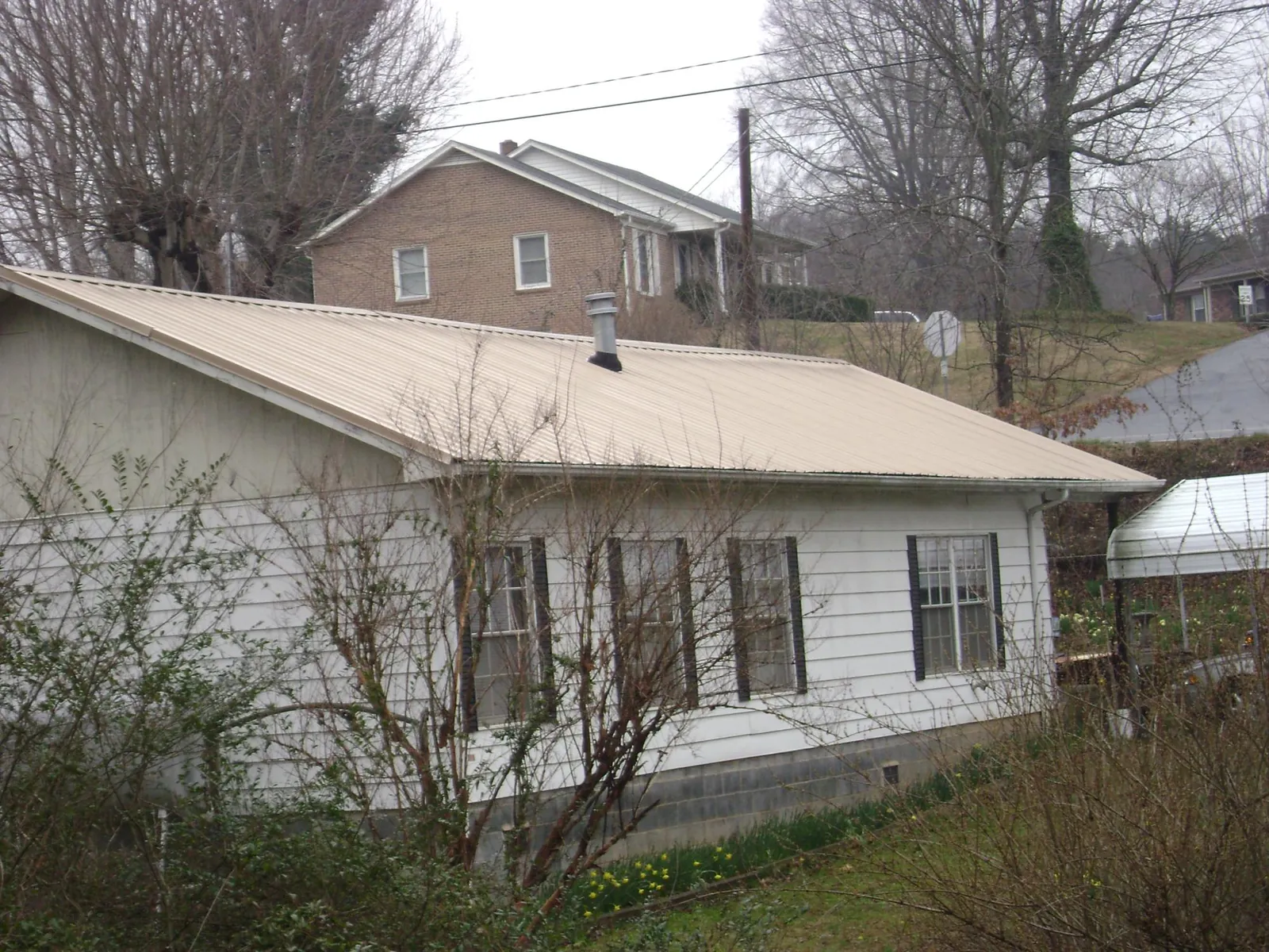 Tan metal roof on a white sided house set into a hillside — Commercial Roofing by Roofing Brothers in Bellmawr